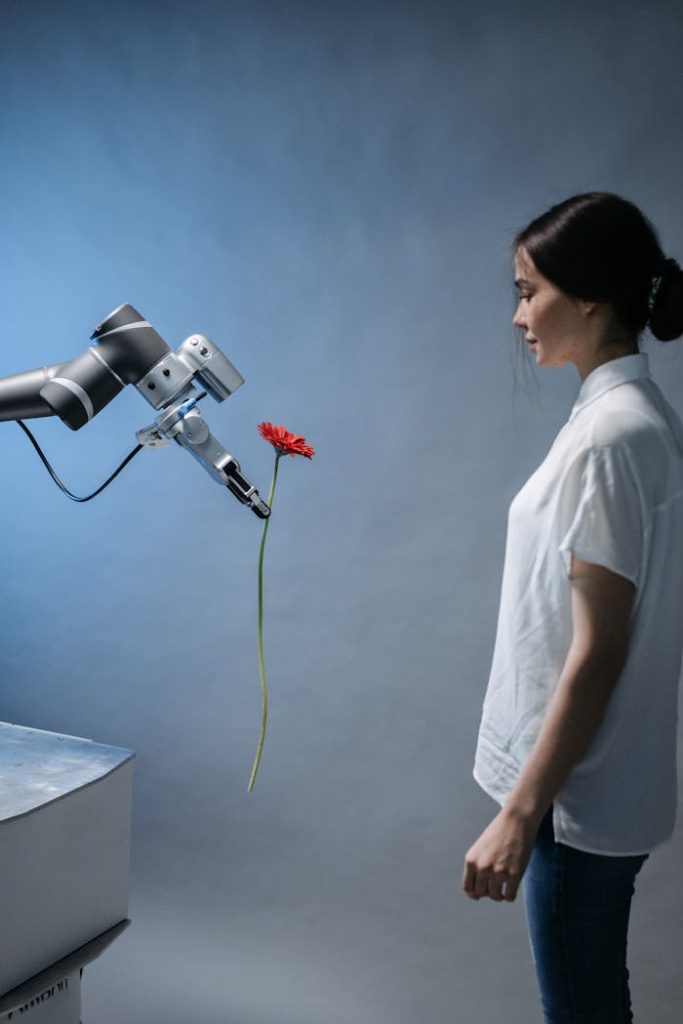 pexels photo 8438965 A woman observes a robot holding a red flower, symbolizing technology and nature integration.